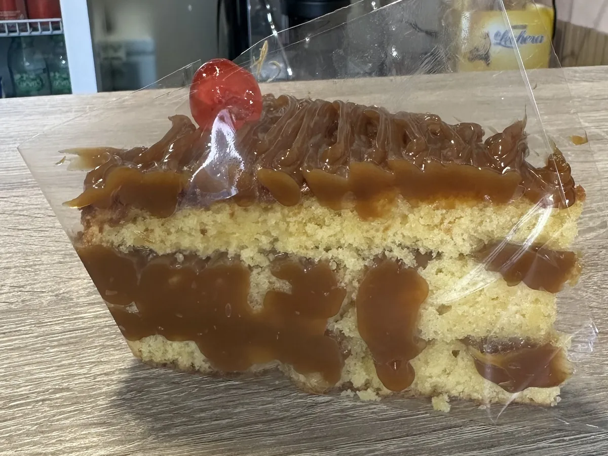 Porción de tarta de vainilla cubierta de dulce de leche, con una guinda encima