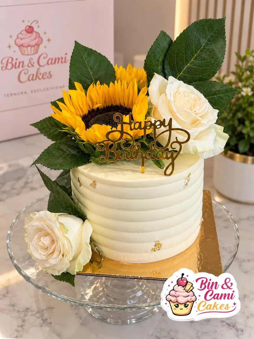 Tarta de cumpleaños de un piso, alta, cubierta de buttercream blanco con textura de rayas horizontales y toques de pan de oro.